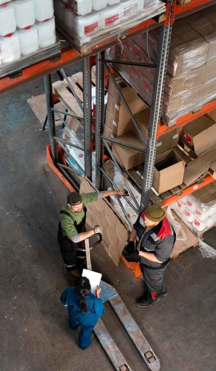 Bezpieczne składowanie i transport towarów – magazyn z pracownikami i zabezpieczonymi paletami w strefie załadunku.